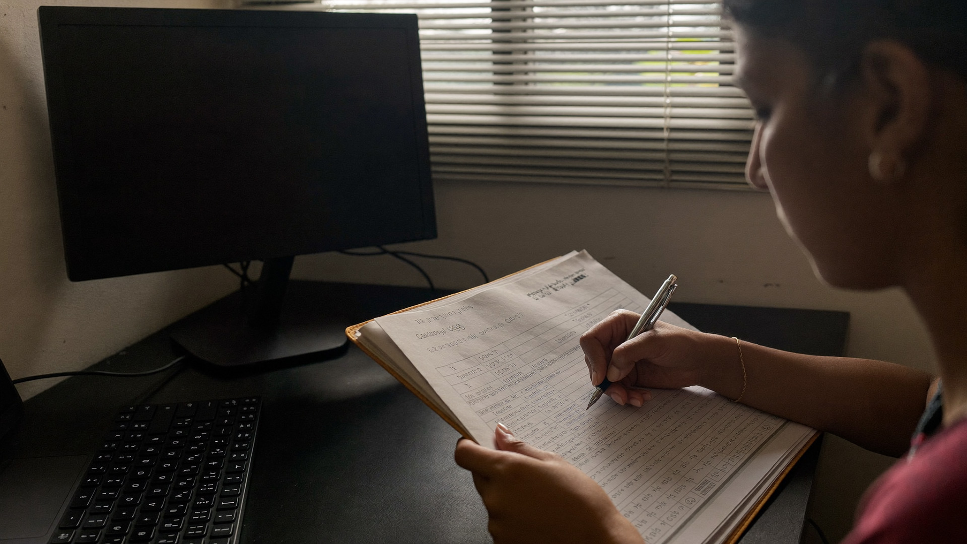 An accounts desk, the new software dark at the edge of the frame while the ledger stays open